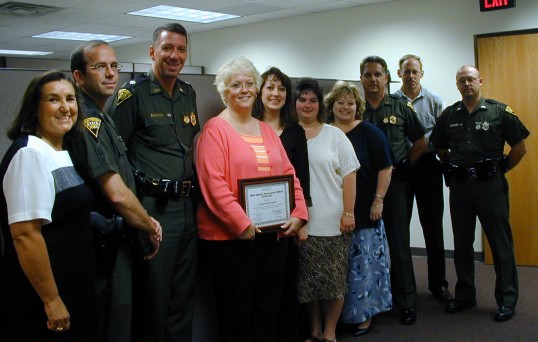 State Police's Carole Woodyard (c) is joined with many of her friends and co-workers at the ceremony conducted at the Purchasing Division.